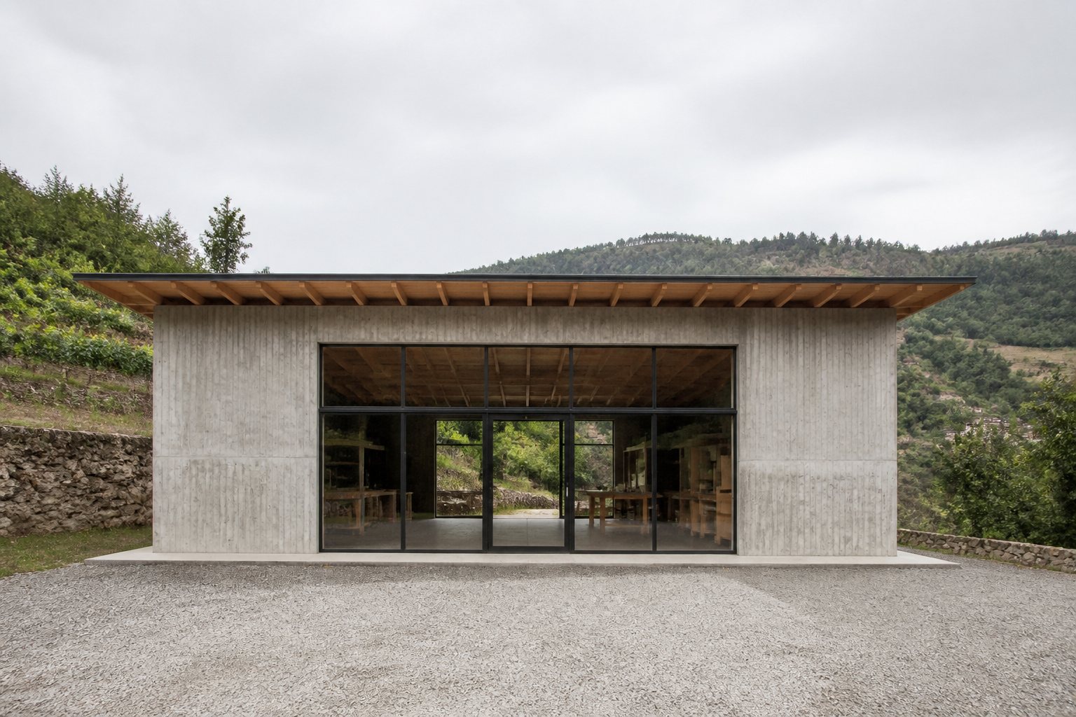 Fotografia ilustrativa de um pavilhão simples em betão e madeira, em meio rural. Imagem de ambiente, não uma obra da empresa.
